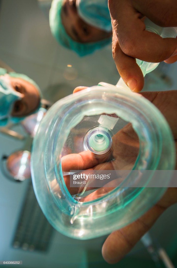 Close up of a doctor about to put an oxygen mask in operating room.